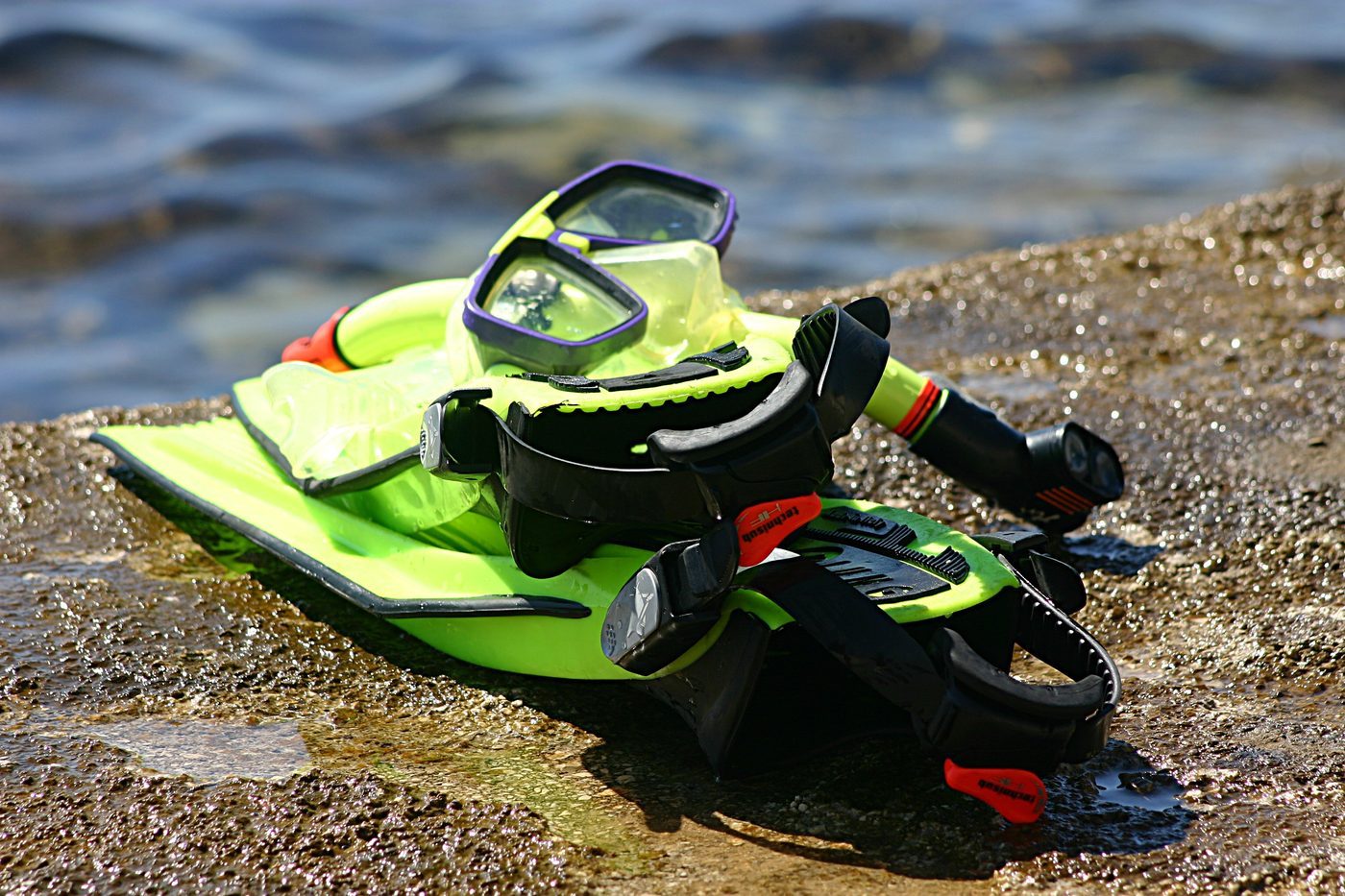 A bright snorkel set with mask, dry snorkel, and fins resting on a rocky Kaua'i shoreline