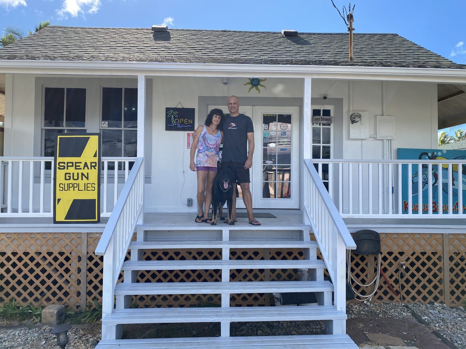 Owners Mike and Janie standing with their dog on the front porch of Kapaa Beach Shop