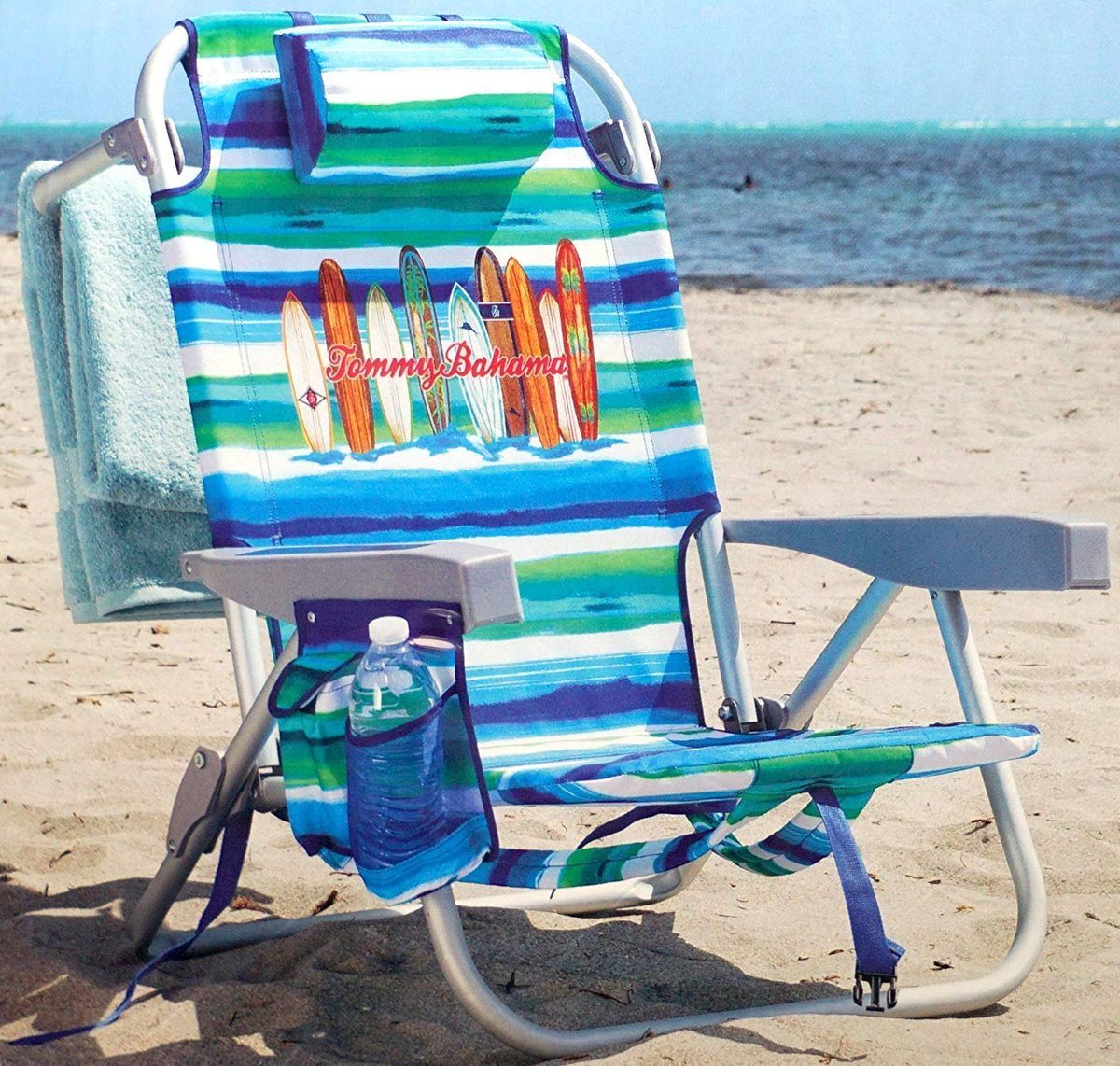 A striped Tommy Bahama backpack beach chair set up on the sand by the water