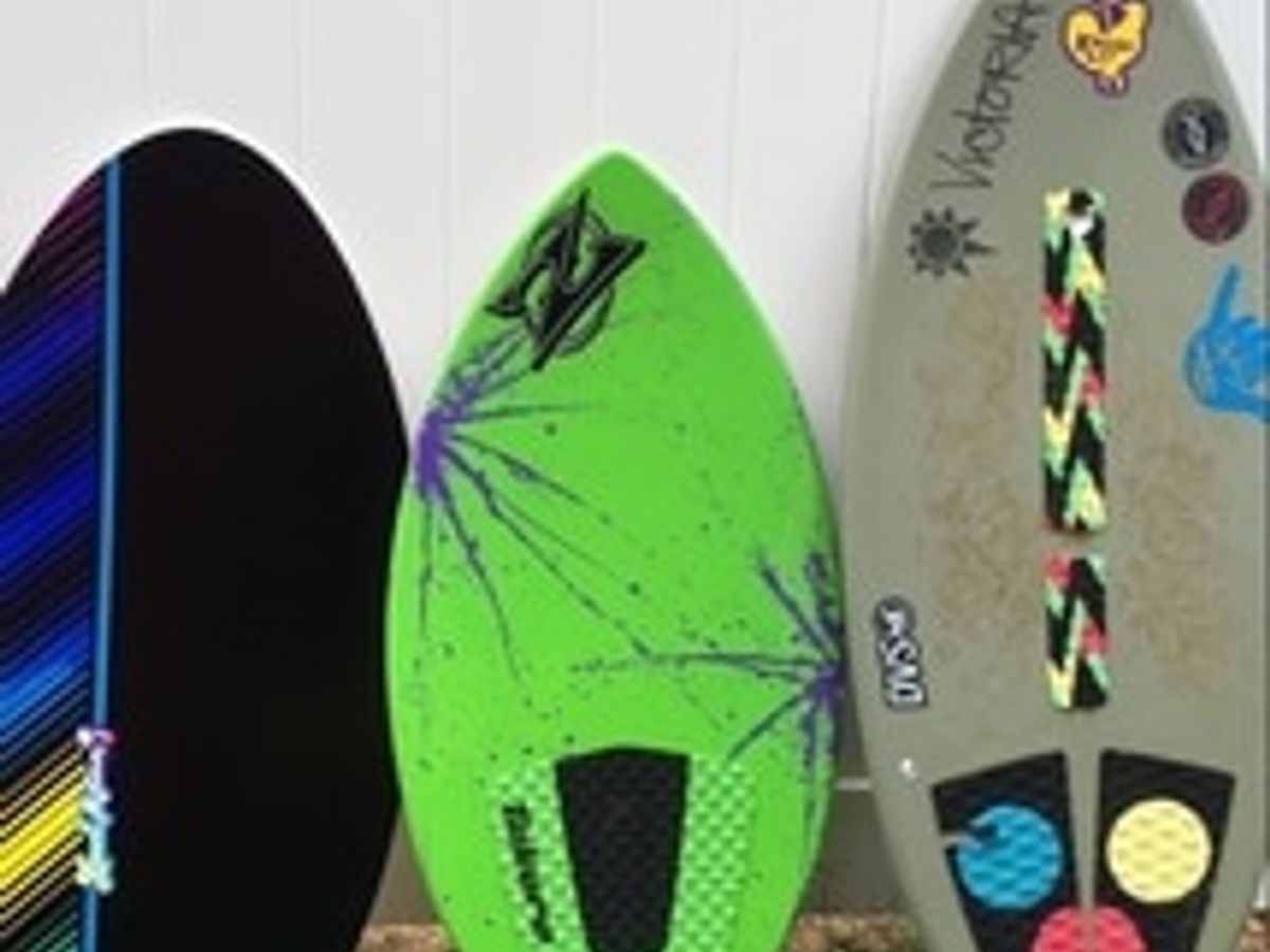 Three fiberglass skim and body boards leaning against a wall, ready to rent