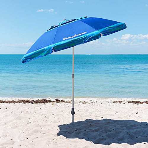 A blue Tommy Bahama beach umbrella planted in the sand on a sunny beach